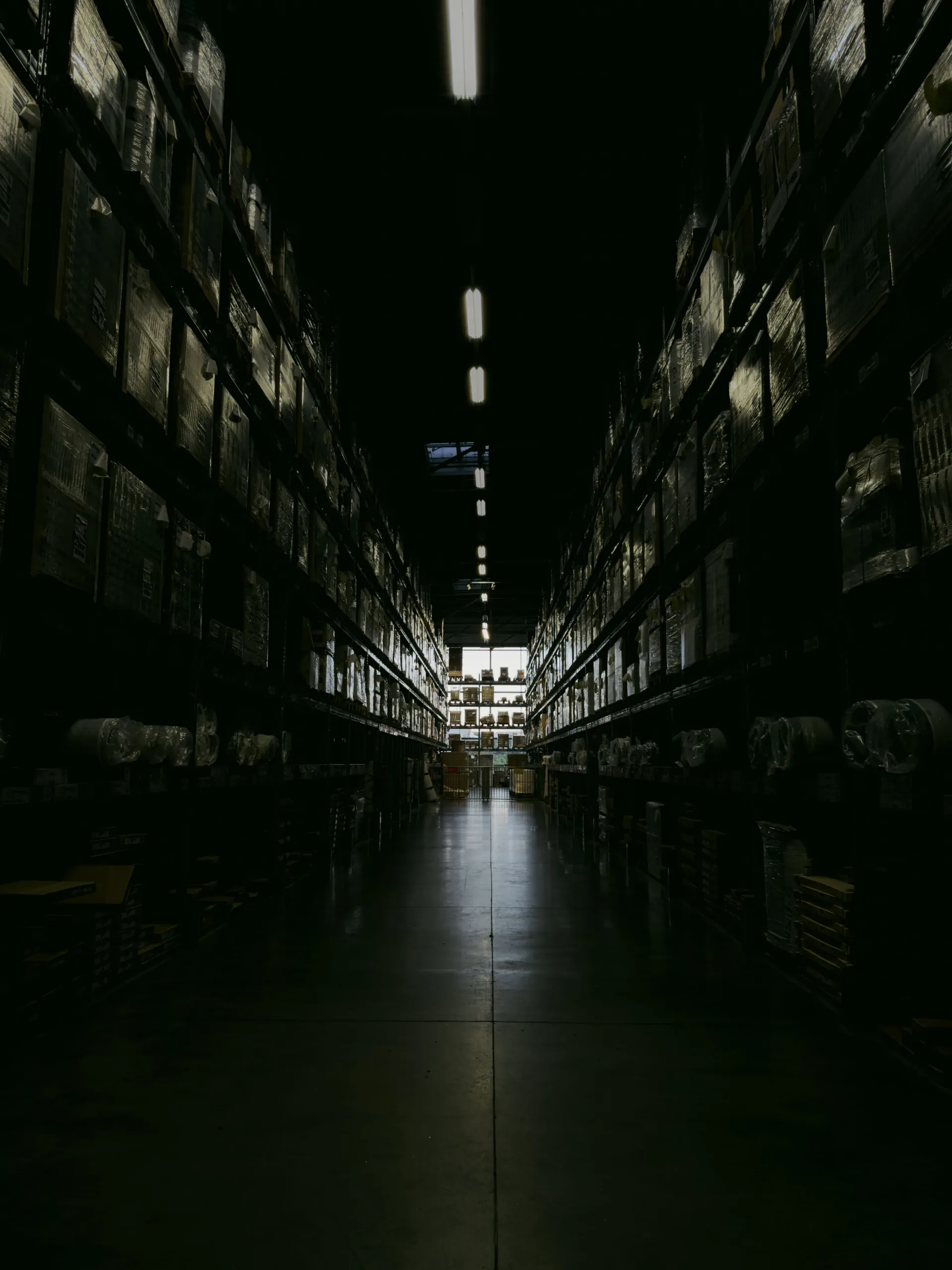 A long, dimly lit warehouse aisle between tall racks